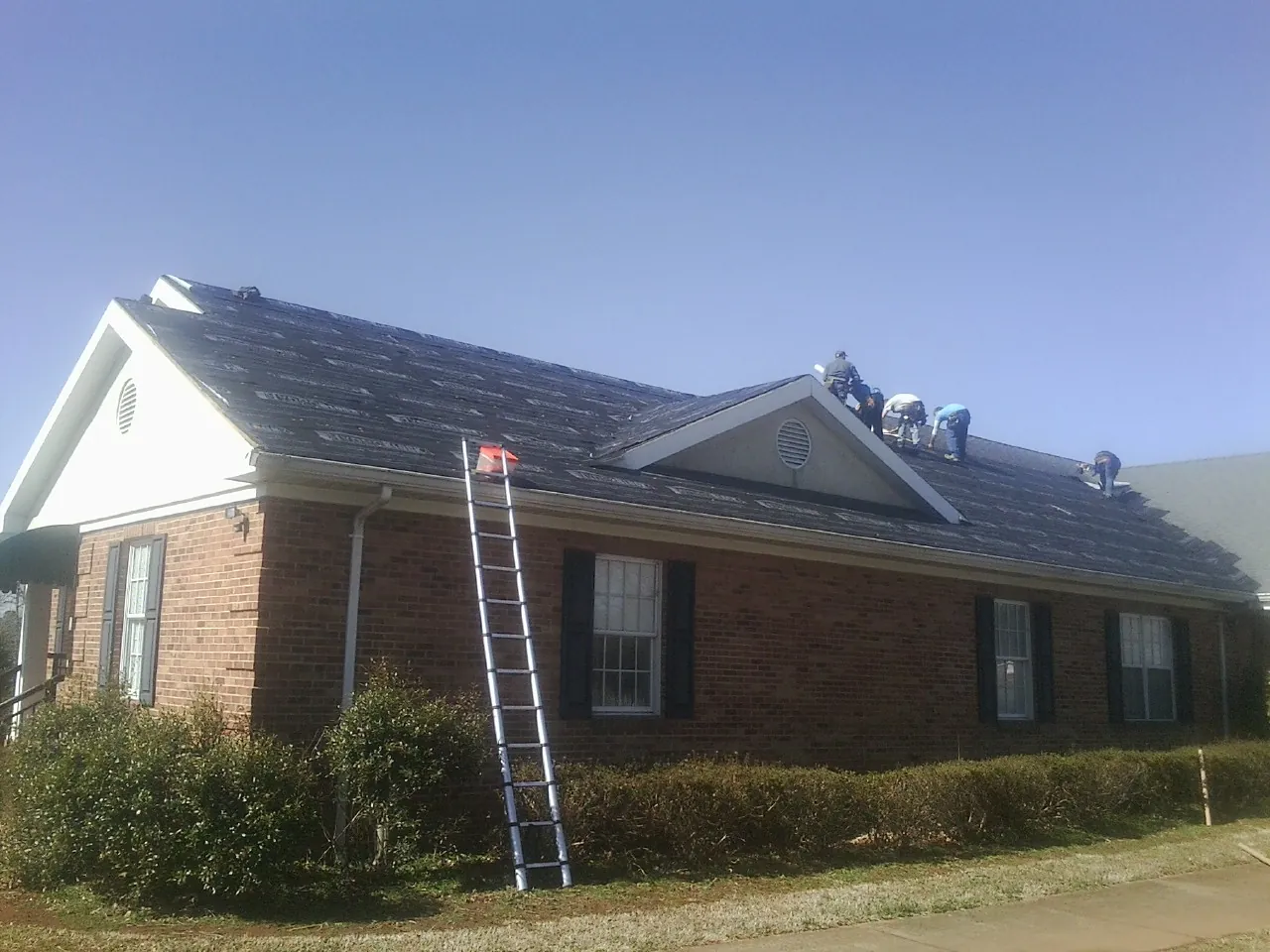 Crew tearing shingles off a brick ranch roof with a ladder set — Metal Roof Repair work by our crew in East Weymouth