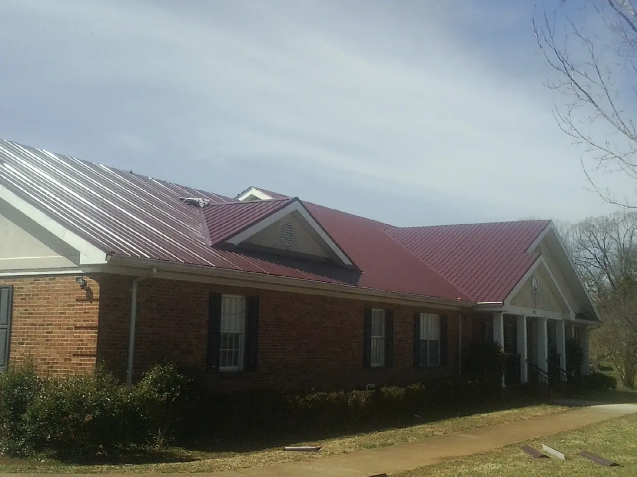 Red metal roof with gabled entries on a long brick building, from a Hail Damage Roof Repair job in East Weymouth