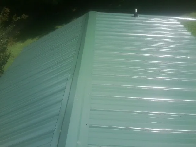 New green metal panels meeting at the ridge of a roof — Flat Roof Repair work by our crew in East Weymouth