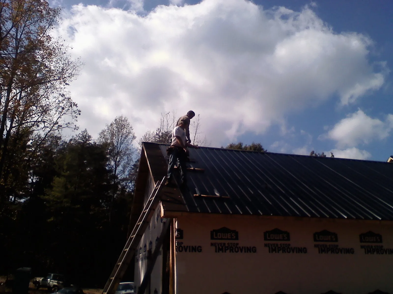Roofer fastening dark metal panels high against a cloudy sky, from a Roof Inspection job in East Weymouth