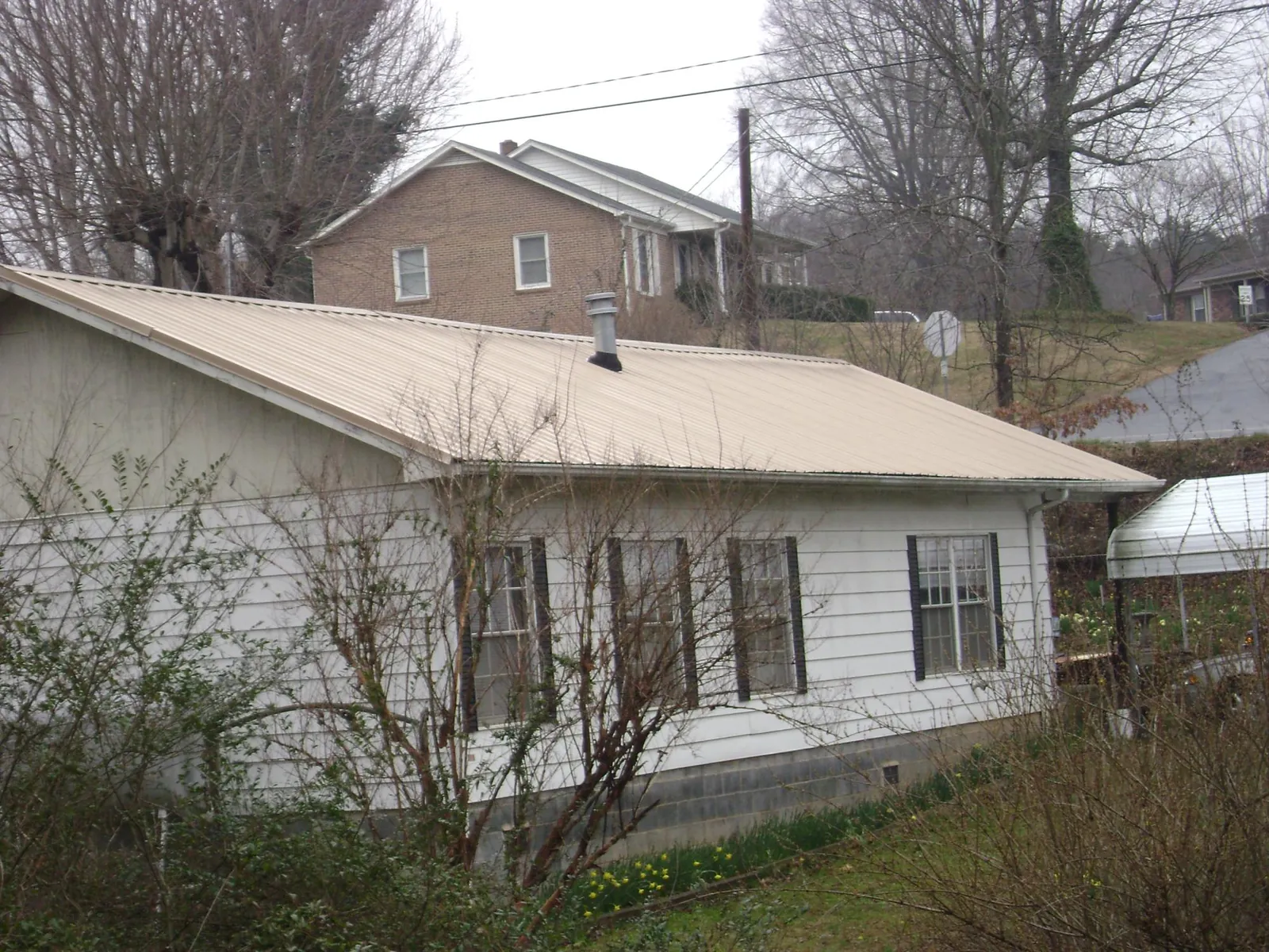 Tan metal roof on a white sided house set into a hillside — Commercial Roofing by Roofing Brothers in East Weymouth